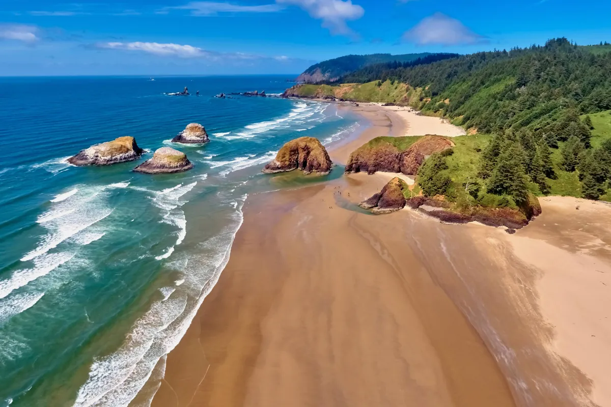A breathtaking view of the ocean waves crashing onto a sandy beach, framed by natural rock formations and lush greenery. Distant hills complete the scene, capturing the natural coastal beauty accessible from the inn's outdoor gathering spaces.