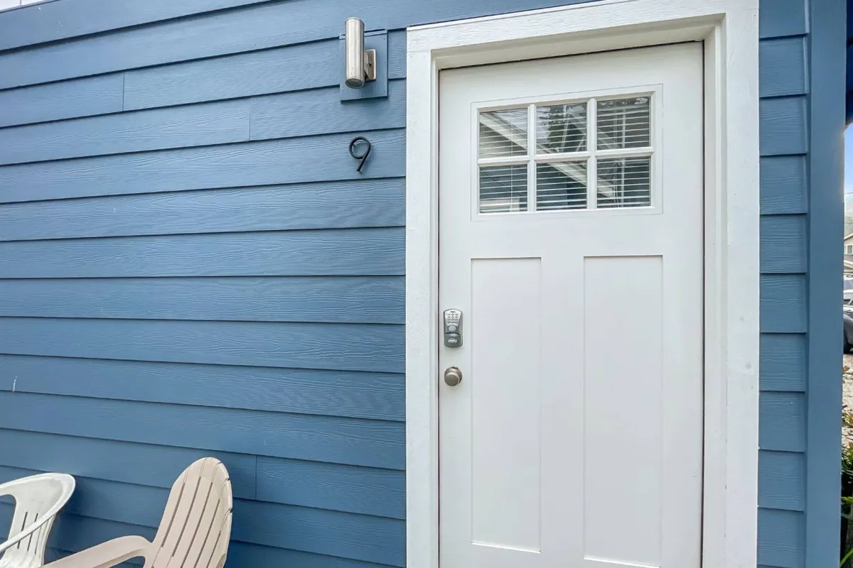 This image captures the inviting studio entrance with a welcoming front door, clearly marked house number, and an adjoining outdoor seating area. The exterior lighting and subtle holiday decor evoke a sense of warmth and arrival, hinting at the blend of private comfort and community found at the property.