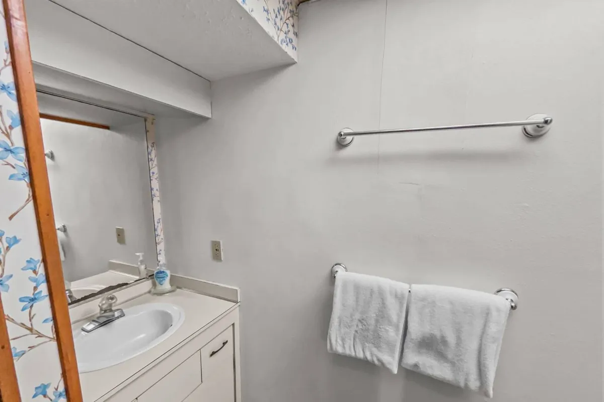 A bright and thoughtfully arranged bathroom corner, featuring a modern sink, a well-lit mirror, plush towels, and subtle wall decor. The space is uncluttered and designed for ease of use, emphasizing comfort and convenience.